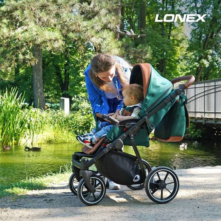 4-5-6-miesięczne dziecko w spacerówce, mama nachyla się nad maluszkiem w parku, ciesząc się wspólnym spacerem w zielonym wózku Lonex Sport.
